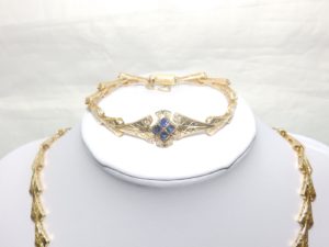 Conjunto de Collar y Brazalete en Oro, con eslabones en V, y rombo central cuajado de "blue strass" y circonitas.