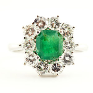 Sortija de oro blanco con esmeralda central y orla de diamantes.
