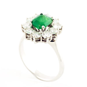 Sortija de oro blanco con esmeralda central y orla de diamantes.